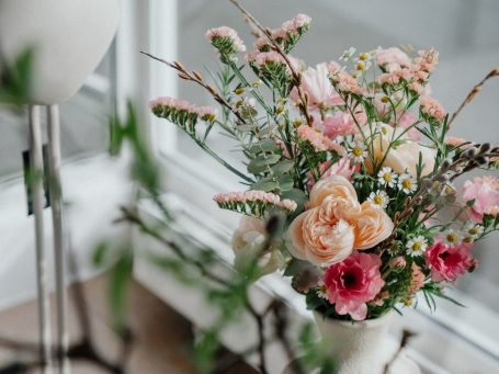 Strauß aus weißen und lila Blumen, darunter Rosen und Lilien, auf einem Holzuntergrund.