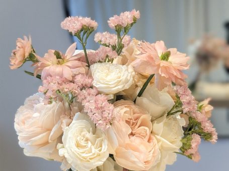 Ein Blütenkranz in Herzform mit einer Trauerschleife und Kerzen im Hintergrund.