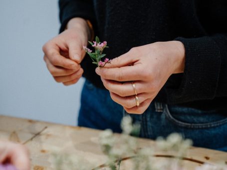 Adventskranz mit grünen Blättern, roten Blüten und goldenen Kerzenhaltern.
