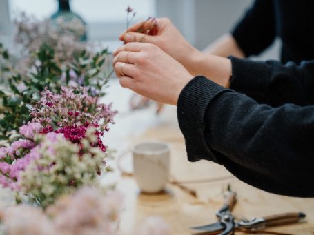 Grüne Pflanzen, rote Beeren und Bindematerial liegen auf einem Tisch.
