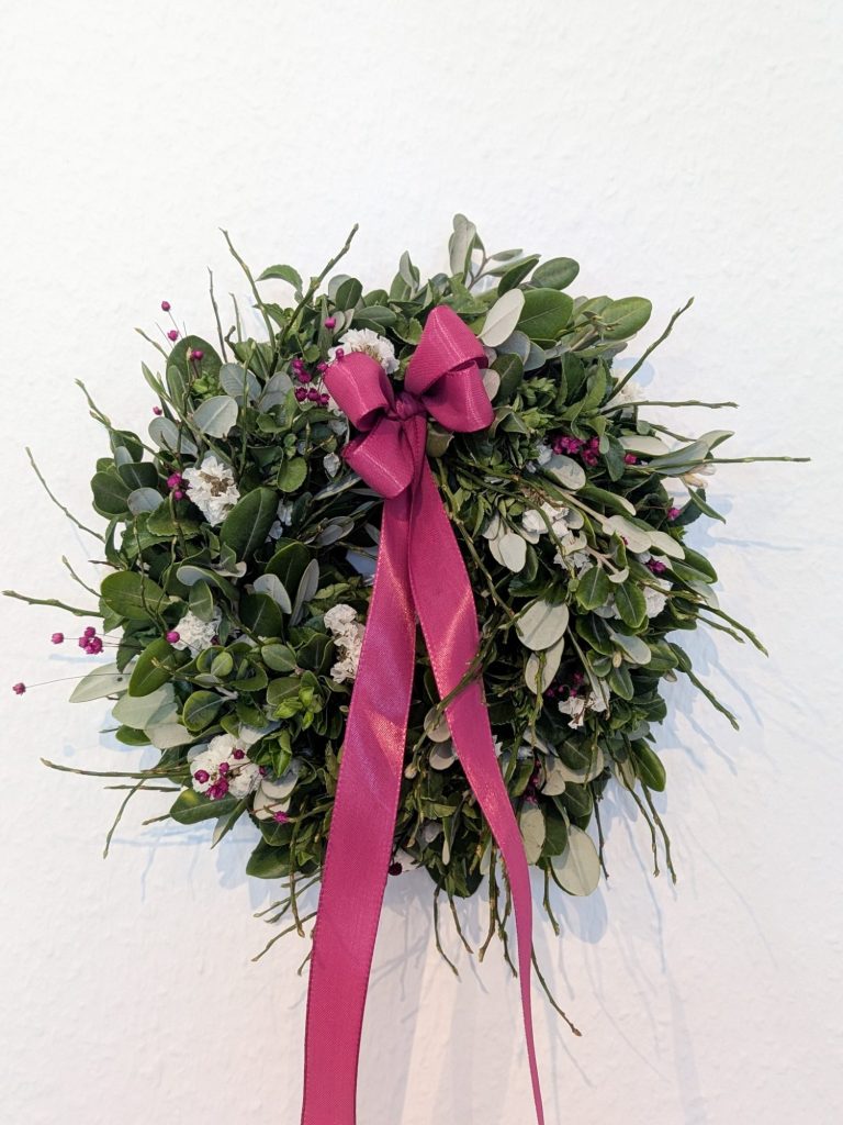 Adventskranz binden Ein festlicher Kranz mit roten Bändern, Tannenzweigen und Dekorationselementen.